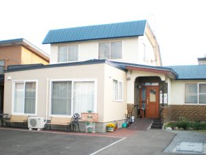 介護施設の建物外観。白壁に青い屋根、玄関には小さなポーチがある